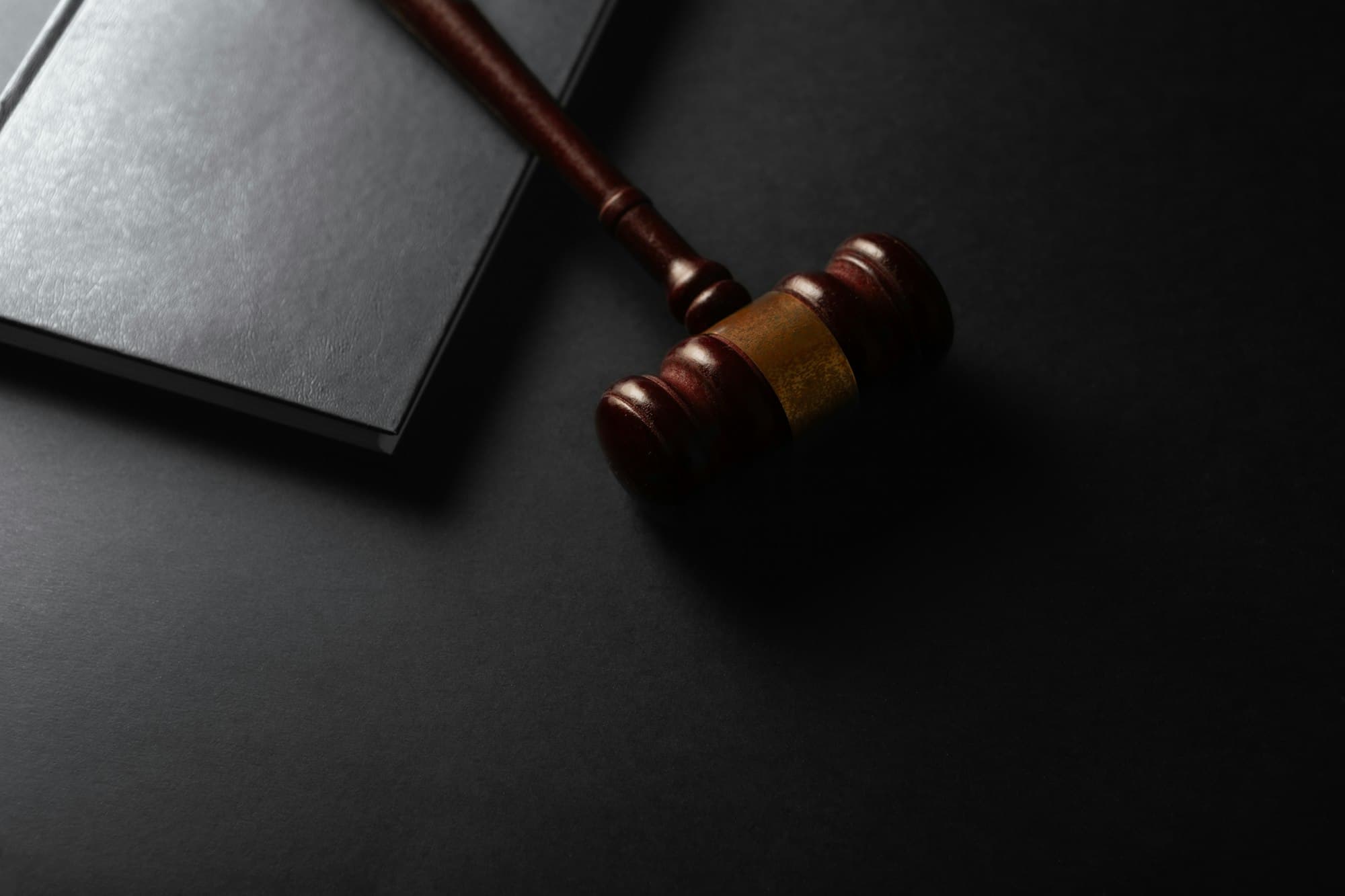 A wooden gavel resting on a dark surface next to a law book