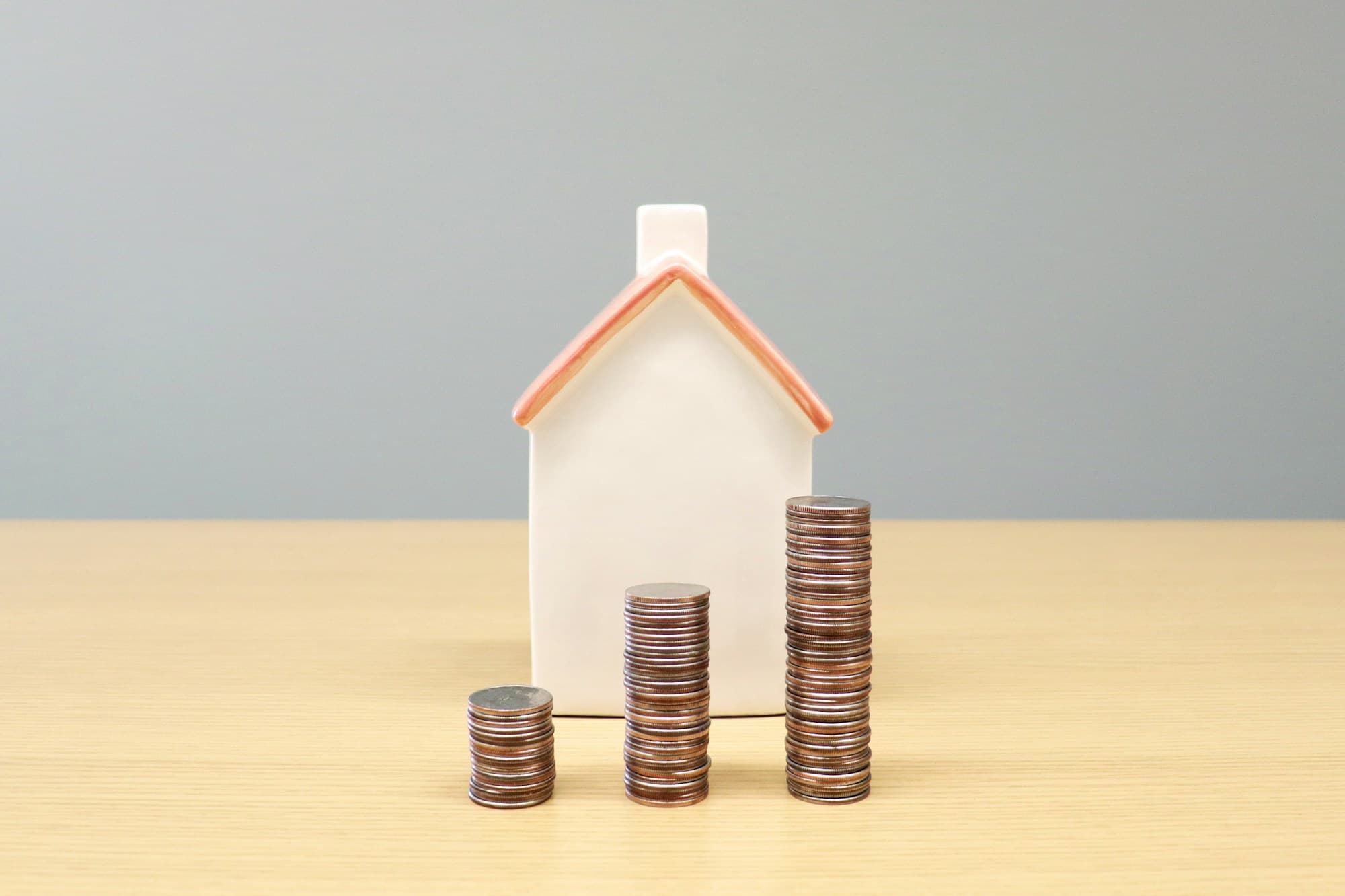 A miniature house and stacks of coins on a table — representing property valuation
