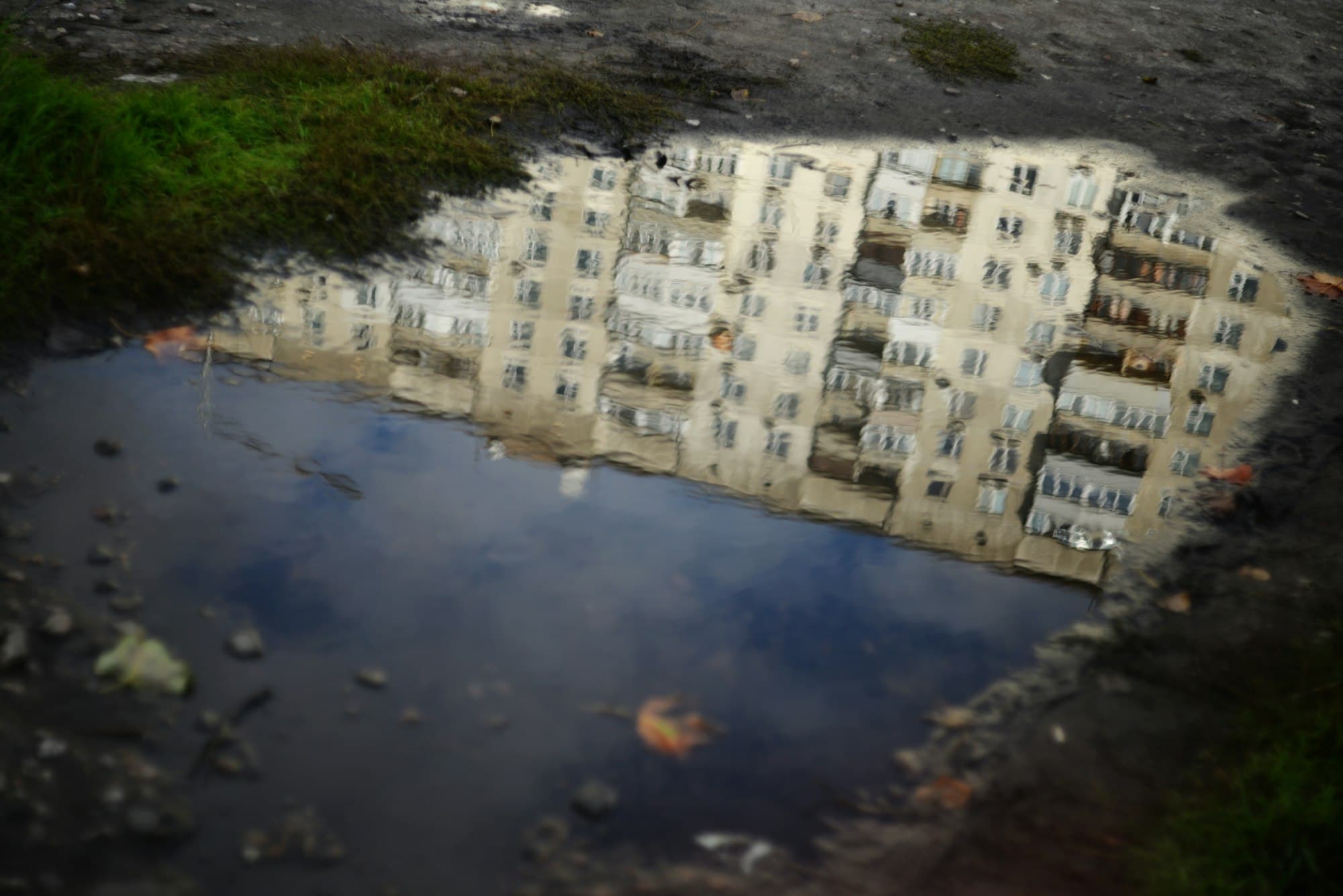 An apartment building reflected in a large puddle of standing water on the ground
